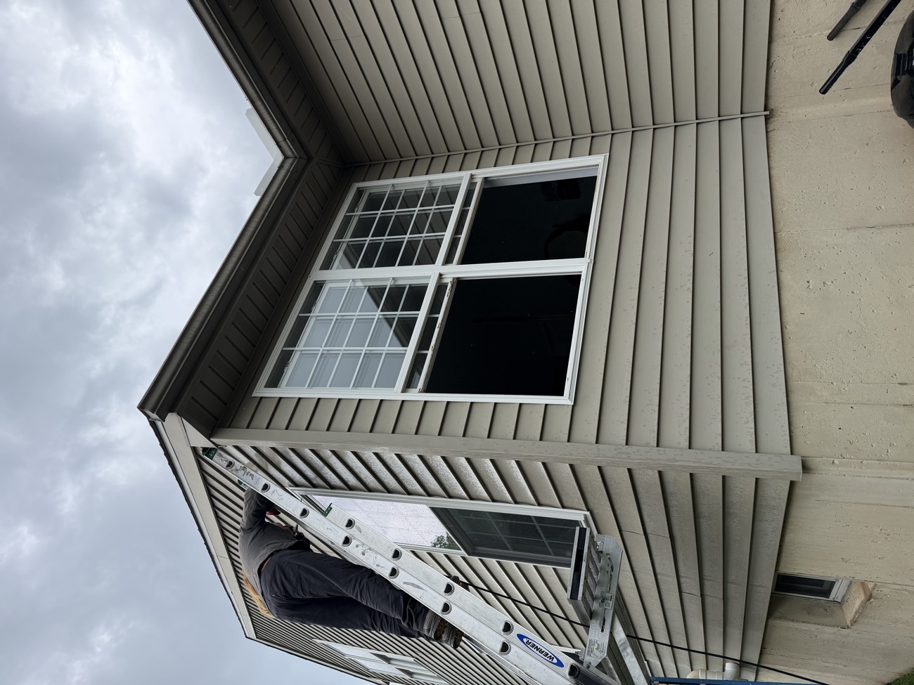Installer on a ladder fitting a large colonial-grid window on the upper storey.